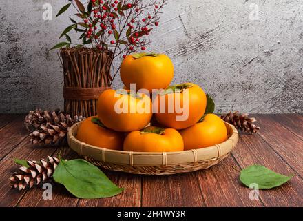 Süße Kaki im Bambuskorb. Mittelspersimon-Set, Vorderansicht, horizontaler Holztisch-Hintergrund. Stockfoto