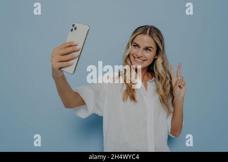 Blonde Teenager-Mädchen zeigt Friedenszeichen, während Selfie auf dem Smartphone Stockfoto