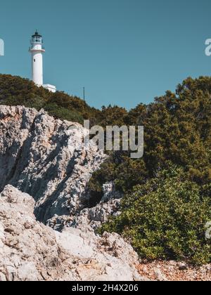 Leuchtturm auf felsigen Klippen mit sommerlicher Vegetation. Strahlend klarer blauer Himmel in Griechenland. Landschaftlich reizvoller Urlaubsort. Insel Lefkada. Vertikal, farblich abgestuft Stockfoto