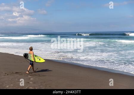 Surfer gouing ins Wasser bei Areal de Santa Barbara - ein hübscher schwarzer Sandstrand an der Nordküste der Insel Sao Miguel, Azoren, Portugal Stockfoto