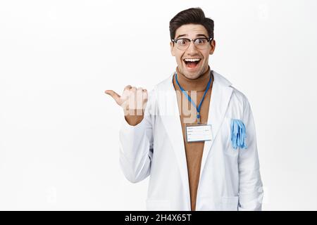 Aufgeregter Arzt in Brille lächelnd, nach links zeigend, Promo-Deal, Werbung auf weißem, isoliertem Hintergrund, männlicher Arzt in Klinik Stockfoto
