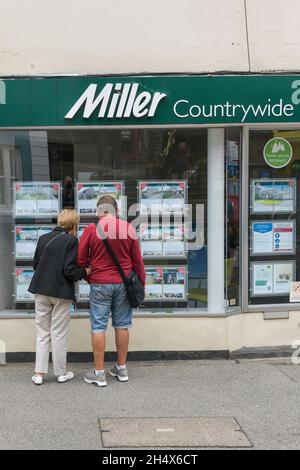 Ein reifes Paar, das sich Immobilien im Fenster eines Miller Countrywide Estate Agents in Falmouth in Cornwall ansieht. Stockfoto