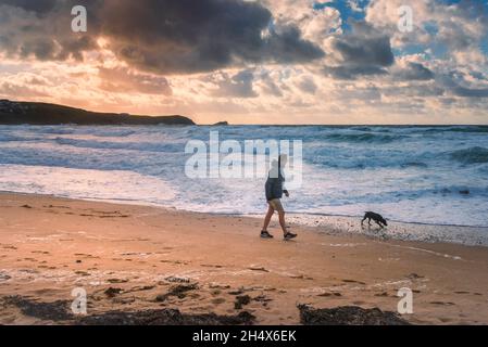 Abendlicht über einem Mann, der mit seinem Hund am Fistral Beach in Newquay in Cornwall entlang der Küste läuft. Stockfoto