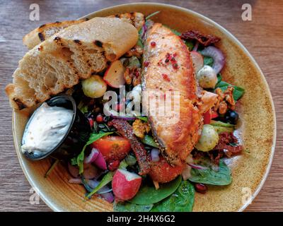 Gesundes, ausgewogenes Mittagessen - gegrilltes Filet aus rotem Fisch, Lachs und Tomaten, Gurken, Oliven, Feta-Zwiebel, Sauce, Blick von oben auf das Brot Stockfoto