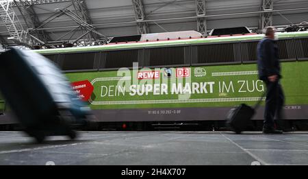 05. November 2021, Hessen, Frankfurt/Main: Passanten gehen an einem Wagen mit der Aufschrift „Hessens Supermarktzug!“ vorbei Während der Präsentation des temporären Projekts 'Fair Supermarket on the Train' im Frankfurter Hauptbahnhof. Der FAIR Supermarktzug ist ein voll funktionaler Supermarkt mit Fairtrade, Bio- und Regionalkost in einem umgebauten Zug. Partner sind Fairtrade, DB Regio und Rewe Region Mitte. Nach dem Start am 5. November 2021 wird der Zug durch sechs hessische Städte fahren. Foto: Arne Dedert/dpa Stockfoto