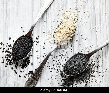 Gesundes Essen und Trinken Konzept. Schwarze und weiße Sesamsamen und Mohnsamen in einem Löffel auf einem Holztisch Stockfoto