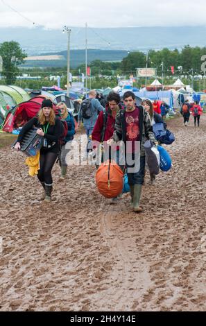 Festivalbesucher, die ihre Campingausrüstung am 08. August 2015 in Kendal, Großbritannien, beim Kendal Calling Festival im Lowther Deer Park durch den Schlamm tragen Stockfoto