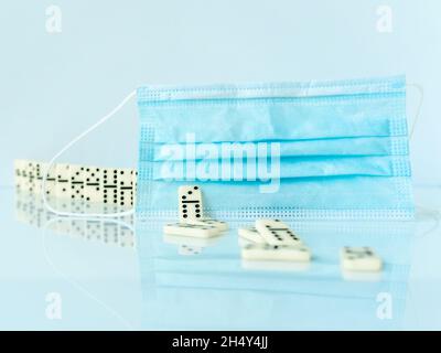 Chirurgische Maske stoppt Dominoeffekt auf weißem Hintergrund. Stockfoto