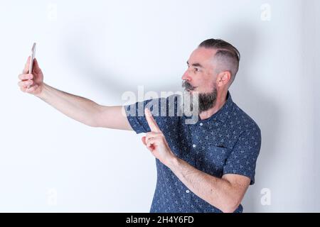 Lustiger bärtiger Hipster-Stil in seinen 40er Jahren, der ein Selfie mit seinen Fingern machte, was auf ein Siegeszeichen hinweist Stockfoto