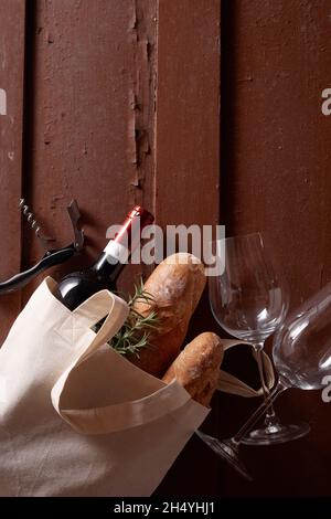 Vertikale Aufnahme von Wein und Baguettes in einer Tragetasche auf rotem Hintergrund mit Korkenzieher und Gläsern Stockfoto