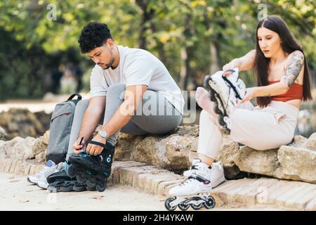 Zwei junge Menschen sitzen auf dem Boden eines Parks und tragen Inline-Skates im Freien Stockfoto