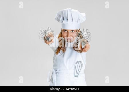 Lustige kleine niedliche Mädchen in weißen Koch Uniform und riesigen Koch Hut isoliert auf weißem Studio Hintergrund. Stockfoto