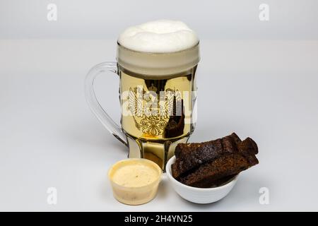 Knoblauchknollen mit Käsesauce und ein Becher mit Bier auf einem weißen Teller. Stockfoto
