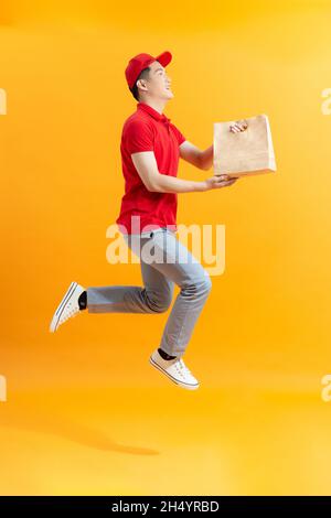 Der Lieferer in roter Uniform hält ein Bastelpapierpaket mit Essen Stockfoto