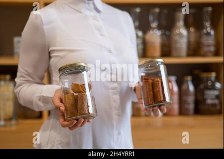 Eine Frau hält ein Glas mit süßen pürierten Fruchtpastila. Süßwaren mit natürlichem Gewicht in einem Ökoladen Stockfoto