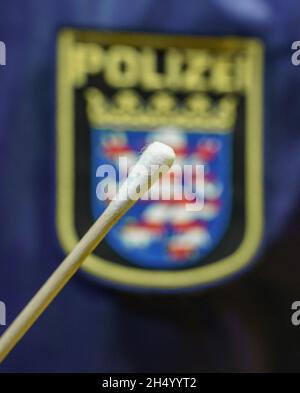 05. November 2021, Hessen, Büdingen: Ein Polizeiangestellter hält heute Nachmittag in der Wolfgang-Konrad-Halle im Kreis Lorbach einen Teststock vor einem hessischen Polizeilogo (symbolisches Bild). Hier findet ab Samstag (06/11/2021) ein serieller DNA-Test auf der Suche nach der Mutter eines toten Säuglings statt, der 1999 gefunden wurde. Die Ermittler hoffen, dass dies ihnen helfen wird, Fortschritte bei der Lösung des mutmaßlichen Tötungsverdachts zu erzielen. Rund 600 Frauen aus der Umgebung der Stadt im Bezirk Wetterau, die zwischen 13 und 30 Jahre alt waren, als die Leiche gefunden wurde, wurden gebeten, freiwillig eine Speichelprobe zu geben. Ph Stockfoto