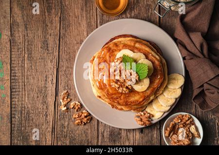 Pfannkuchen mit Banane, Nüssen und Honig auf Holzgrund. Draufsicht, Kopierbereich. Stockfoto