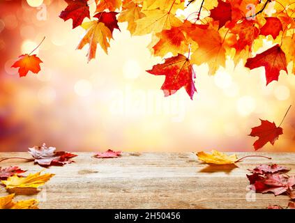 Holztischplatte auf verwackelte Herbsthintergrund. Herbst goldenen abstrakten Hintergrund mit Bokeh Licht und bunten Blättern. Schöne Herbstblätter fallen auf Stockfoto