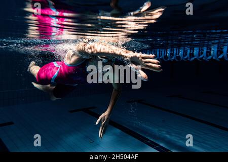 Unterwasseraufnahmen. Eine Schwimmerin trainiert im Hallenbad. Unterwasseransicht der Schwimmbewegungen Details. Stockfoto