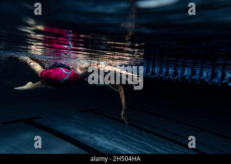 Unterwasseraufnahmen. Eine Schwimmerin trainiert im Hallenbad. Unterwasseransicht der Schwimmbewegungen Details. Stockfoto