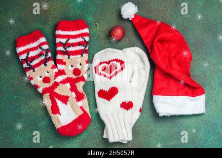 Weihnachtszubehör von Santa Claus - Fäustlinge, Socken mit Hirsen und roter Hut auf festlichem grünen Hintergrund. Weihnachtskarte. Draufsicht Stockfoto