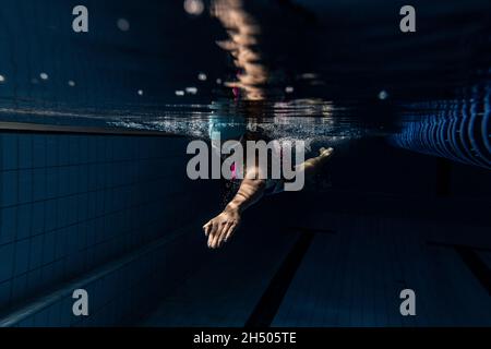 Unterwasseraufnahmen. Eine Schwimmerin trainiert im Hallenbad. Unterwasseransicht der Schwimmbewegungen Details. Stockfoto