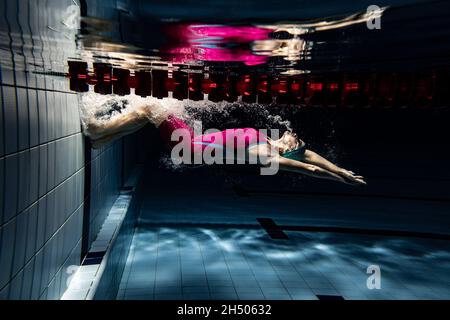 Unterwasseraufnahmen. Eine Schwimmerin trainiert im Hallenbad. Unterwasseransicht der Schwimmbewegungen Details. Stockfoto