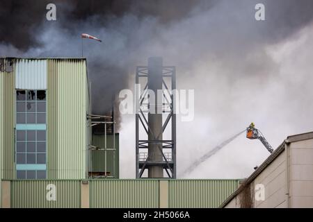 Hannover, Deutschland. November 2021. Von einer Drehleiter löschen Feuerwehrleute das Feuer in einem Industriegebäude am Brinker Hafen, aus dem schwarzer Rauch aufsteigt. Quelle: Moritz Frankenberg/dpa/Alamy Live News Stockfoto