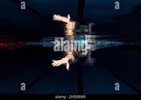 Professionelle Schwimmerin in Badekappe und Schutzbrille in Bewegung und Aktion während des Trainings am Pool, drinnen. Unterwasseraufnahmen Stockfoto