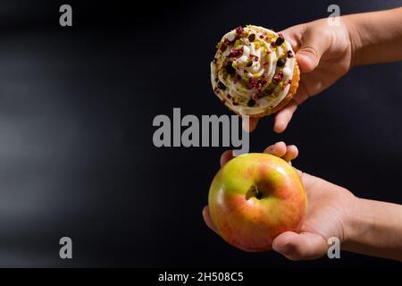 Kinderhände, die die Wahl zwischen Apfel und süßem Cupcake auf Schwarz mit Kopierfläche treffen. Stockfoto