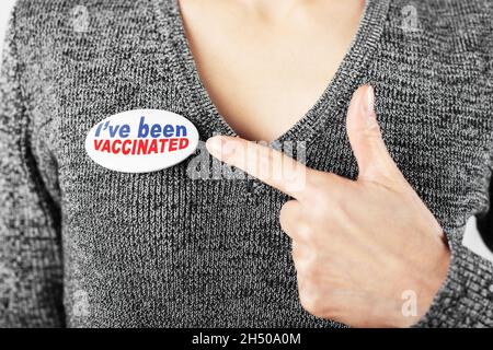 Kaukasische Frau mittleren Alters in grauem Pullover, der mit dem Finger auf die Knopfleiste mit dem Text zeigt, dass ich geimpft wurde Stockfoto