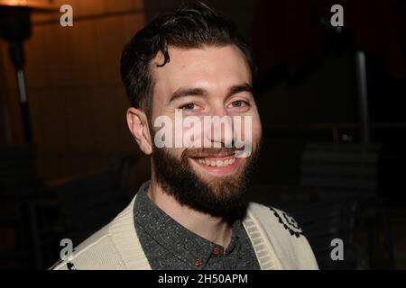 Der weißbärtige Mann sitzt abends in einem Restaurant mit unterschiedlichen Gesichtsausdrücken. Stockfoto