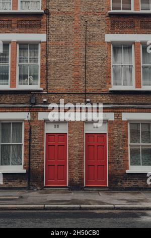 London, Großbritannien - 17. Oktober 2021: Traditionelle rote Eingangstüren an einem Apartmentblock in Victoria-Gebäuden in Southwark, London. Die Türen sind in hellen Farben Stockfoto