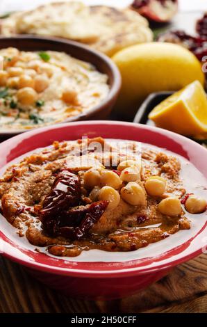 Frischer hausgemachter Hummus in Tonform mit Olivenöl, Kichererbsen, Gewürzen und sonnengetrockneten Tomaten auf Steintisch Stockfoto