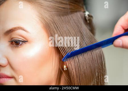 Friseur glättet weibliche braune Haare von mittlerer Länge mit einem Haar mit einem Eisen Haarglätter und Kamm in einem Schönheitssalon Stockfoto