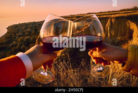 Zwei Gläser mit Rotwein in ausgestreckten Händen und Belgorod Dnestrovsky Canyon im Hintergrund Stockfoto