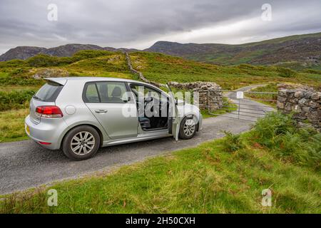 Das Auto wartet darauf, dass ein Tor auf einer eingezäunten Straße in den Hügeln von Nord-Wales in der Nähe von Harlech geöffnet wird. Stockfoto