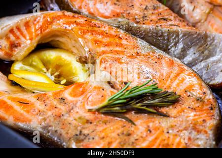 Frisch geröstete Fischsteaks aus rotem Lachs mit Kräutern, Gewürzen und Zitrone auf schwarzem Metallteller in der Küche. Stockfoto