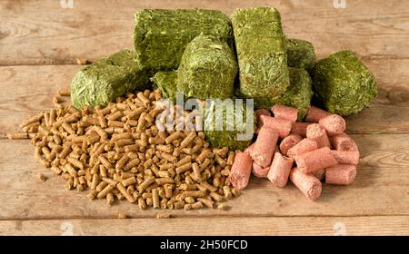 Pellettierfutter links, grüne Alfalfa-timothy-Würfel in der Mitte und rosa Pfefferminzbonbons rechts auf rustikalem Holztisch Stockfoto