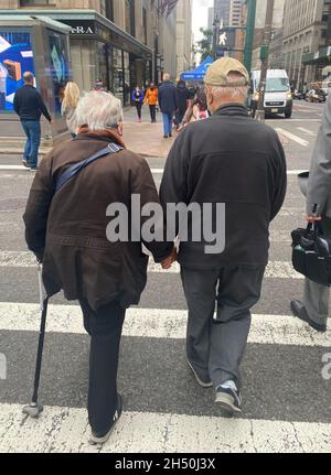 Das Seniorenpaar überquert im Herbst Hand in Hand die 42nd Street entlang der 5th Avenue in Midtown Manhattan. Stockfoto