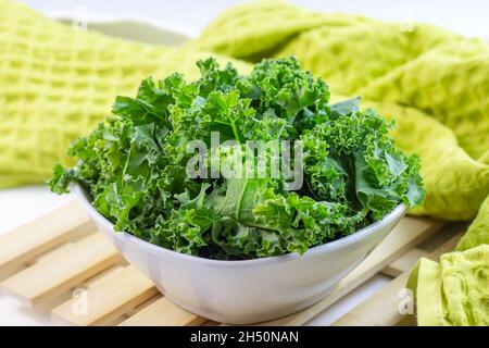 Frisches grünes Lockenkohl oder Grünkohl-Salatblätter, die auf hellem Hintergrund auf dem Tisch in der Küche in die Schüssel geschnitten werden. Stockfoto