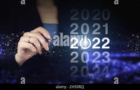 2022 Neujahr. Hand hält digitale Grafik Stift und Zeichnung digitale Hologramm 2022 Zeichen auf Stadt dunkel verschwommen Hintergrund. Konzept Start Neujahr 2022 Stockfoto