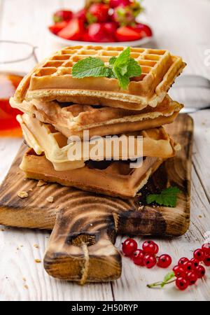 Stapel von belgischen Waffeln auf Schnittbrett mit Erdbeeren und Sirup beiseite Stockfoto