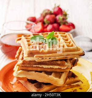 Haufen belgischer Waffeln auf weißem Holzküchentisch mit Erdbeeren und Sirup beiseite Stockfoto