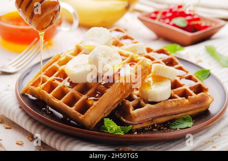 Hausgemachte knusprige belgische Waffeln mit Banane und Honig serviert Stockfoto