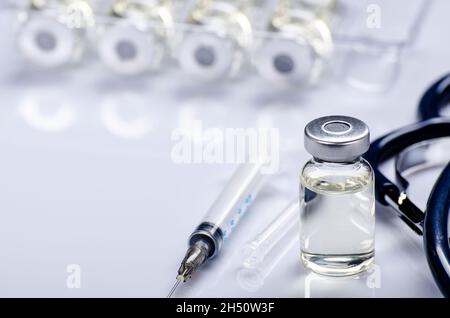 Fläschchen mit flüssigem Medikament als Impfdosis Grippeimpfung zusammen mit Stethoskop, Spritze für Injektionsbehandlung auf medizinischem Tisch. Impfung oder Immunisierung c Stockfoto