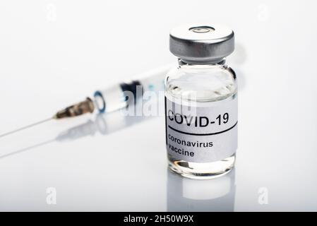 Glasfläschchen mit Etikett für Coronavirus-Impfstoff zusammen mit Nahaufnahme der Spritze Stockfoto