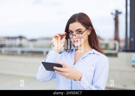Junge Nerd Rotschopf kaukasischen Geschäftsfrau hält Smartphone im Freien Stockfoto