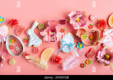Easter mattierte Kekse in Form von Hühnchen und Kaninchen, Zuckerstreuseln, Süßigkeiten, Ausstechformen auf rosa Hintergrund. Flaches Lay-Mockup Stockfoto