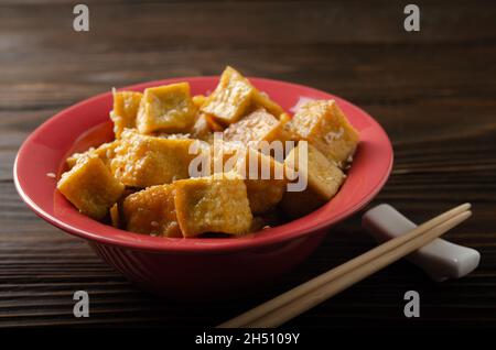 Knusprig frittierte Tofu-Würfel in Tonform auf einem hölzernen Küchentisch Stockfoto